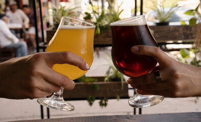 Celebration. Two young women hands toasting with beer cups filled with amber ale and golden honey beer.