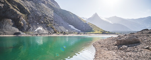 Blue turquoise lake Kulikalon against the backdrop of rocky mountains with glaciers on a warm sunny morning in the Fan Mountains in Tajikistan, landscape in the mountains - obrazy, fototapety, plakaty