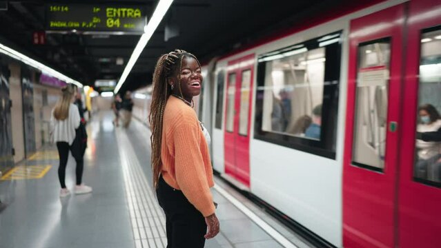 Young African woman with vitiligo, joyfully standing at subway station. Female broad smile and relaxed body language convey her comfort and happiness with the convenience of urban public transport
