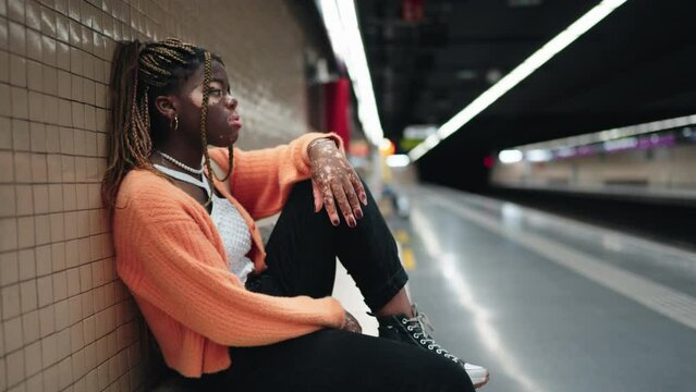 Young African woman with vitiligo sitting at subway station,  challenges common during teenage years. Black female student living her adolescent experience with hormonal mood swings
