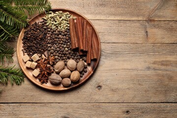 Different spices, nuts and fir branches on wooden table, flat lay. Space for text