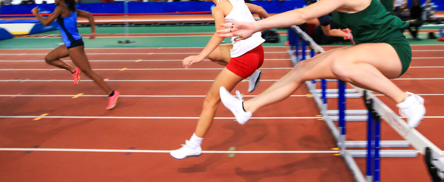 Girls running over hurdles indoors