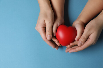 Mother and her child holding red decorative heart on light blue background, top view. Space for text