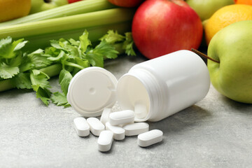 Dietary supplements. Overturned bottle and pills near food products on grey textured table