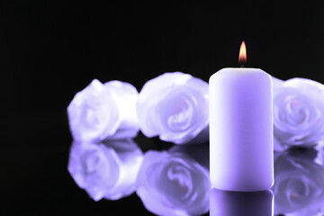 Violet roses and burning candle on black mirror surface, space for text. Funeral attributes