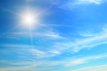 cumulus clouds and a bright sun in the blue sky.
