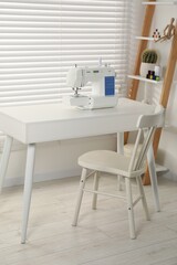 Fototapeta na wymiar Sewing machine on white desk near chair indoors