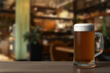 Mug with fresh beer on wooden table in pub, space for text