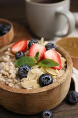 Tasty oatmeal with strawberries, blueberries and almond flakes in bowl on wooden table, closeup