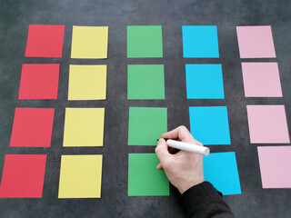 Hand writing on a colorful array of sticky notes on a grey background.