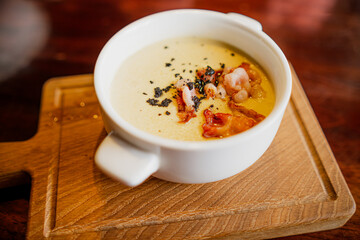 A bowl of soup is placed on a wooden cutting board, showcasing a simple yet comforting meal.