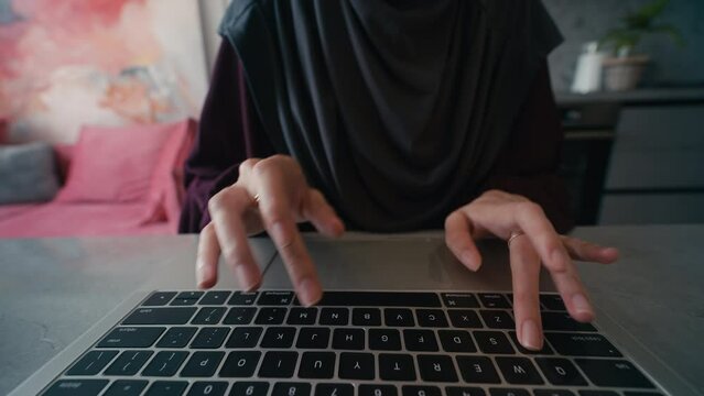 Close-up hands of Arab woman working on computer, using keyboard and touchpad