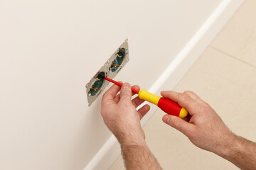 Man installing electrical outlet on the wall with a screwdriver - 761723477