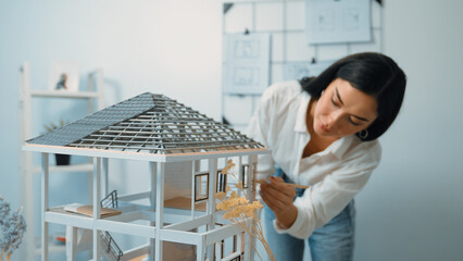 Young beautiful caucasian architect engineer turns house model around to inspect house construction...