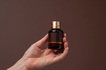 Close-up of hand holding luxury elegant skincare product bottle on a rich chocolate brown isolated...