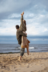 An exhilarating moment of a woman being lifted in the air by a man on the beach, both exuding...