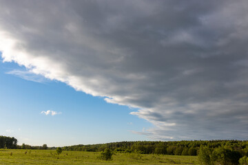 Sunny landscape against a dramatic sky, countryside in early spring, young green grass in a field