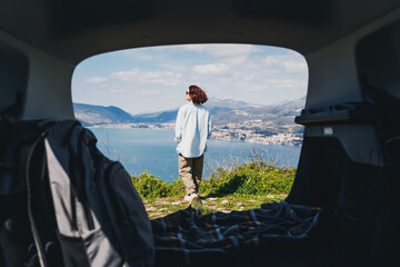 A young woman traveling by car admires the view of the sea and mountains, summer vacation auto travel concept. Shot through the car - 761733658
