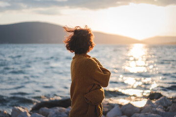 Smiling young woman in a yellow sweater looking at view at sunset enjoy sunshine. - 761734215