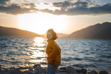 Smiling young woman in a yellow sweater looking at view at sunset enjoy sunshine. - 761734455