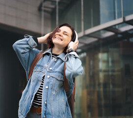 Young Caucasian happy cheerful woman in headphones listening to music and walking - 761734603