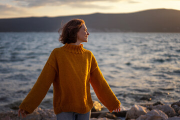 Smiling young woman in a yellow sweater looking at view at sunset enjoy sunshine. - 761735801