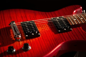 Red wood electric guitar close up, dramatically lit isolated on black background.