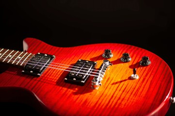 Red wood electric guitar close up, dramatically lit isolated on black background.