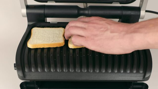 Toasting bread in the electric grill. Women's hands place bread on the grill. The concept of toasting bread.