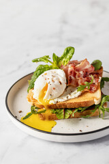 Toasts sandwich with poached egg, arugula, bacon and cream cheese on white plate marble background. Isolated, text space