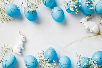 Happy Easter background with blue eggs, rabbits, spring flowers on stone table. Flat lay, top view, copy space.