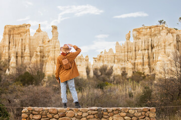A man in a brown jacket and hat stands on a bridge looking out over a canyon