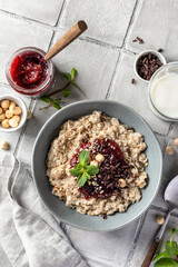 Oatmeal porridge with raspberry jam and nuts in gray bowl on gray tile background served with spoon, top view. Healthy diet breakfast