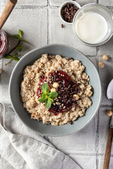 Oatmeal porridge with raspberry jam and nuts in gray bowl on gray tile background served with spoon, top view. Healthy diet breakfast