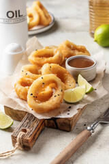Crisp fried golden squid rings with lemon and sauce on wooden board, light background