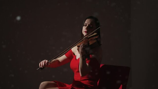Portrait Of Female Violinist In Red Dress Playing Romantic Melody In Studio, Snowflakes Flying Up