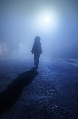 The silhouette of a little girl walking down a misty street.