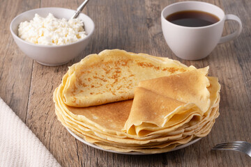 A stack of thin pancakes, a plate with cottage cheese and coffee