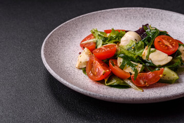 Delicious fresh caprese salad with mozzarella, tomatoes, greens with salt, spices and herbs