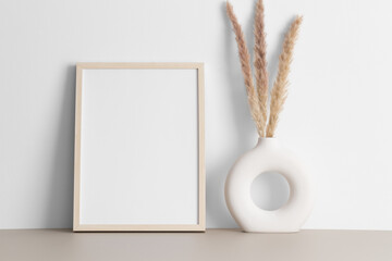 Wooden frame mockup with a pampas decoration on the beige table.