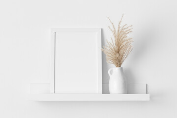 White frame mockup with a pampas decoration on the wall shelf.