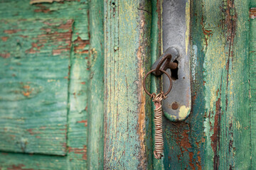 Old lock with a rusty key with a worn green painted wooden surface