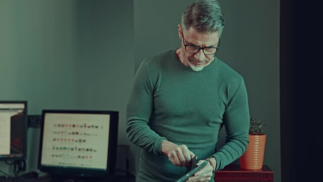 Older man working with tablet computer in home office. Mid adult male in glasses, happy, smiling, looking busy. Casual businessman in office.