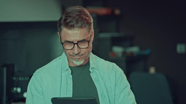Man working on tablet computer in office, looking at screen. Portrait of mid adult busy businessman in work place.