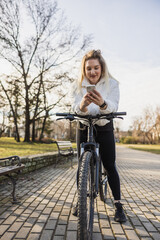 Woman Using Smartphone While Leaning on a Bicycle at a Park