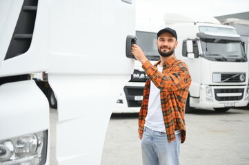 Portrait of young bearded man standing by his truck. Professional truck driver standing by semi...