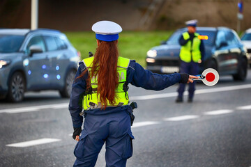 Policjantka ruchu drogowego z lizakiem podczas zatrzymania pojazdów na drodze z tarczą do zatrzymywania.
 - obrazy, fototapety, plakaty