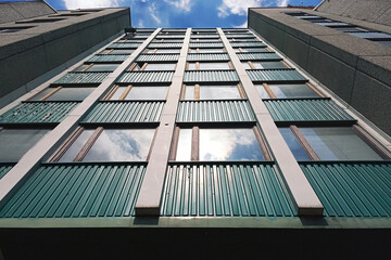 Fototapeta premium Wall of a multi-storey building with reflection of the sky and sunlight in one of the windows exterior. High building in the city, view from below. Office building with sky. 