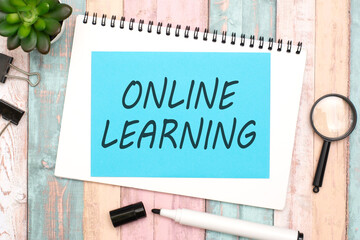 text 'ONLINE LEARNING' on blue paper composition with stationery on color pink background. top view