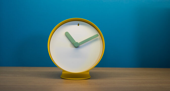 A colorful clock sits on a shelf in front of a blue wall. the hands are green and there are no numbers on the face to tell time. 